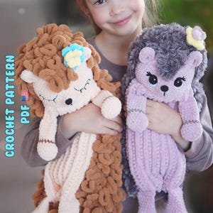 May include: Two plush crochet hedgehogs. One is brown and cream with a blue and yellow flower. The other is lavender with gray accents and a yellow flower. The text "CROCHET PATTERN PDF" is visible on the left side of the image.