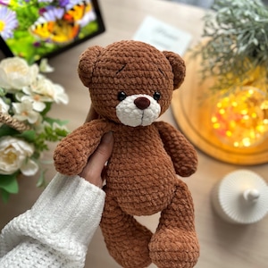 Puede incluir: Un oso de peluche marr&oacute;n hecho a mano con hocico blanco y nariz marr&oacute;n. El oso est&aacute; hecho de un material suave y texturizado y tiene orejas peque&ntilde;as y redondas. El oso est&aacute; sostenido por una persona que lleva un su&eacute;ter blanco. El oso mide aproximadamente 25 cm de alto.