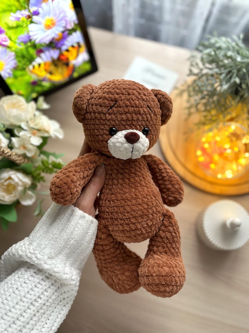 Puede incluir: Un oso de peluche marr&oacute;n hecho a mano con hocico blanco y nariz marr&oacute;n. El oso est&aacute; hecho de un material suave y texturizado y tiene orejas peque&ntilde;as y redondas. El oso est&aacute; sostenido por una persona que lleva un su&eacute;ter blanco. El oso mide aproximadamente 25 cm de alto.