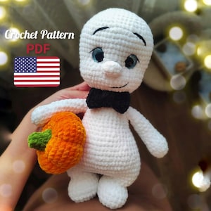 May include: A handmade white crochet ghost doll with a black bow tie and blue eyes, holding an orange pumpkin with a green stem. The image includes the text "Crochet Pattern PDF" and the American flag.