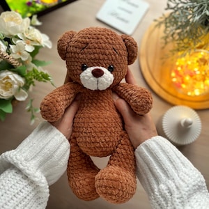 Puede incluir: Un oso de peluche marr&oacute;n hecho a mano con hocico blanco y ojos marr&oacute;n oscuro. El juguete de peluche est&aacute; sostenido por una persona que lleva un su&eacute;ter blanco. El oso tiene un dise&ntilde;o cl&aacute;sico con rasgos redondeados.