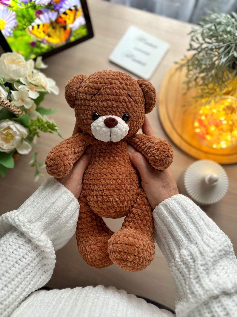 Puede incluir: Un oso de peluche marr&oacute;n hecho a mano con hocico blanco y ojos marr&oacute;n oscuro. El juguete de peluche est&aacute; sostenido por una persona que lleva un su&eacute;ter blanco. El oso tiene un dise&ntilde;o cl&aacute;sico con rasgos redondeados.