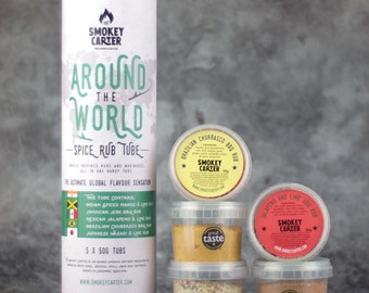 Op de afbeelding: Een set van vijf kruidenwrijfbuizen, elk met een ander smaakprofiel. De buizen zijn gelabeld met de namen van de smaken: Indian Spiced Mango & Lime Rub, Jamaican Jerk BBQ Rub, Mexican Jalapeno & Lime Rub, Brazilian Churrasco BBQ Rub en Japanese Wasabi & Lime Rub. De buizen zijn in piramidevorm gerangschikt op een grijs oppervlak. De tekst op de buis luidt "Around the World - Spice Rub Tube - World Inspired Rubs and Marinades - All in One Handy Tube - The Ultimate Global Flavor Sensation".