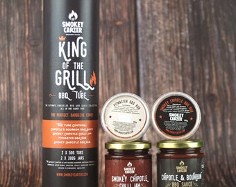 Op de afbeelding: Een zwarte tube met de tekst "King of the Grill BBQ Tube" en het Smokey Carter logo. De tube bevat een verscheidenheid aan BBQ-kruiden en -sauzen, waaronder Smokey Chipotle Chilli Jam, Chipotle & Bourbon BBQ Sauce, Pitmaster BBQ Rub en Smokey Chipotle BBQ Rub.