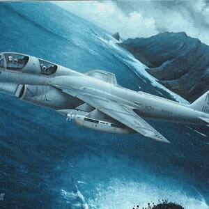 May include: A gray and white military aircraft, a Grumman EA-6B Prowler, flies over a blue ocean with a mountain range in the background. The aircraft has the tail number "NJ 151780" and the number "907" on the side.