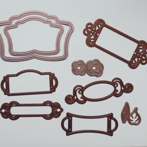 May include: A collection of die-cut metal frames and embellishments in shades of brown. The set includes various shapes: ornate rectangular frames, oval frames, and decorative floral accents. These crafting supplies are ideal for scrapbooking and card making.