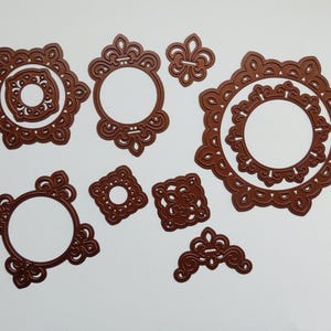 May include: A collection of die-cut decorative frames and embellishments in various shapes, including circles, squares, and a fleur-de-lis. The die cuts are a rich, warm brown color and feature intricate, ornate designs, perfect for paper crafting and scrapbooking projects.
