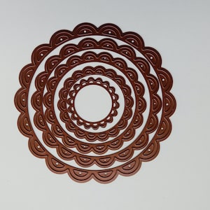 May include: A set of six nested, die-cut circles with a scalloped edge. The die cuts are a warm brown color and are arranged concentrically on a white background. The smallest circle is in the center.