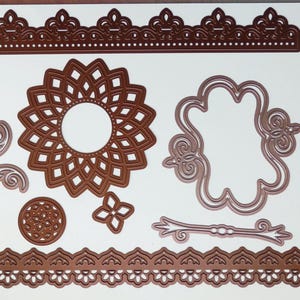 May include: A collection of die-cut shapes in various designs, including a large floral element, decorative borders, and ornate frames. The shapes are a warm brown color and are arranged on a white background.