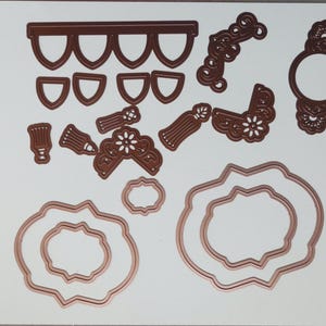 May include: A collection of die-cut shapes in a copper color, including ornate frames, decorative borders, and floral accents. The set includes various sizes and designs, perfect for crafting projects. The shapes are arranged on a white background.