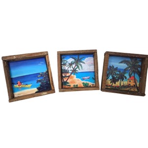 May include: Three square framed paintings depicting tropical beach scenes. Each painting features a wooden frame. The paintings show palm trees, blue water, and a yellow kayak. One painting has a small boat.