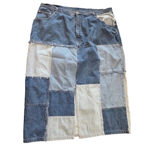 May include: A midi-length denim skirt featuring a patchwork design with varying shades of blue, from light wash to dark indigo. The skirt includes a front button and zipper closure, belt loops, side pockets, frayed seams, and a front slit with studs.