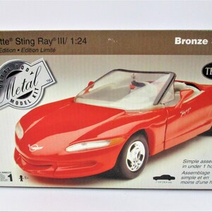 May include: A red 1:24 scale model kit of a Corvette Sting Ray III convertible. The box features the Testors logo and the words "Metal Body Metal Model Kit" in a silver circle. The box also says "Bronze Series" and "Limited Edition - Edition Limité".