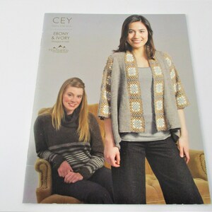 May include: A crochet pattern book featuring two women, one wearing a gray cardigan with brown and white crochet squares and the other wearing a brown and gray striped sweater. The book cover features the title "CEY Ebony & Ivory Designs by Knit Mountaintop".