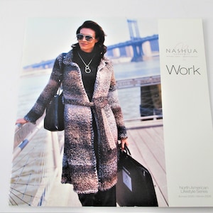 May include: A woman wearing a long, brown and gray knit cardigan with a black turtleneck shirt and sunglasses. She is standing on a pier with a bridge in the background. The image is from a catalog for Nashua Home Fashions, titled "Work" and featuring the North American Lifestyle Series.