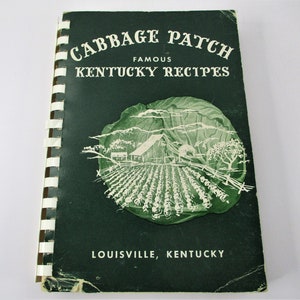 May include: A vintage green cookbook titled "Cabbage Patch Famous Kentucky Recipes" with a black and white illustration of a cabbage patch and a farmhouse on the cover. The book is bound with a white spiral binding.