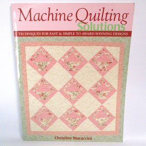 May include: A book titled "Machine Quilting Solutions: Techniques for Fast & Simple to Award-Winning Designs" by Christine Maraccini. The cover features a pink and green quilt with a floral pattern.