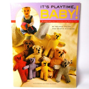 May include: A book titled "It's Playtime, Baby!" with a photo of a baby holding a colorful block and a group of knitted teddy bears in various colors. The book features 9 knit designs for mom and tot.