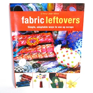 May include: A book titled "fabric leftovers: Simple, adaptable ways to use up scraps" by D'Arcy-Jean Milne. The cover features a colorful collage of fabric scraps, buttons, and beads.
