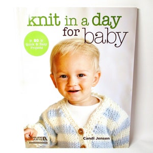 May include: Book cover featuring a baby wearing a blue and white striped knitted cardigan. The title of the book is "Knit in a Day for Baby" with a green circle that says "80 Quick & Easy Projects". The author is Candi Jensen.