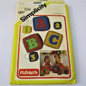 May include: A vintage Simplicity sewing pattern for making Play-School blocks. The pattern includes instructions for making blocks with letters and numbers. The pattern cover features a photo of two children playing with the blocks. The pattern number is 6261.