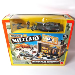 May include: A Matchbox Military Police MP-41 Headquarters 13-piece fold-up playset in a yellow and camouflage box. The packaging features a clear window displaying a toy tank and three small soldier figurines, with graphics of the set in action.