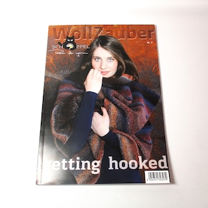 May include: A magazine cover featuring a woman wearing a colorful shawl. The magazine title is "WollZauber" with the text "getting hooked" at the bottom. The cover has a warm color palette with shades of brown, blue, and orange.
