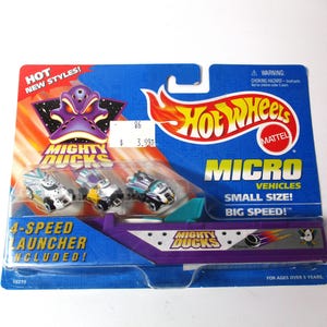 May include: A Hot Wheels Mighty Ducks Micro Vehicles set. The packaging is blue and purple, with the Hot Wheels logo and the text "Micro Vehicles, Small Size, Big Speed!" The set includes a 4-speed launcher.
