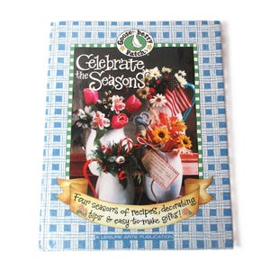 May include: A book titled "Celebrate the Seasons" with a blue and white checkered cover. The cover features a floral arrangement in a white pitcher with red, white, and blue accents. The book is a Leisure Arts Publication.