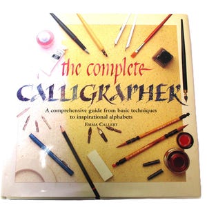 May include: The Complete Calligrapher book with calligraphy tools. The book cover is yellow with the title in red and blue script. The image includes pens, brushes, ink, and a pencil, suggesting a guide to calligraphy.