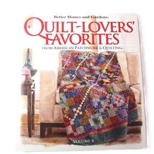 May include: A book titled "Quilt-Lovers' Favorites" from American Patchwork & Quilting, Volume 8. The cover features a colorful quilt draped over a chair in a watercolor style.