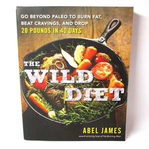 May include: Book cover with a photo of a cast iron skillet filled with meat, vegetables, and herbs. The title of the book is "The Wild Diet" and the author is Abel James. The book cover text says "Go beyond Paleo to burn fat, beat cravings, and drop 20 pounds in 40 days."