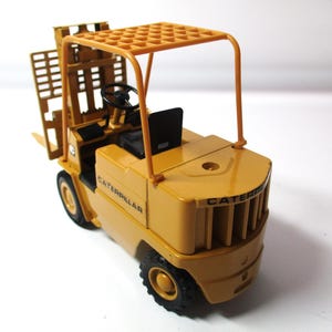 Może przedstawiać: Ż&oacute;łta zabawka w&oacute;zka widłowego Caterpillar z czarnymi oponami i czarnym siedzeniem. W&oacute;zek widłowy ma ochronną konstrukcję nad głową, a na boku widnieje napis "CATERPILLAR".