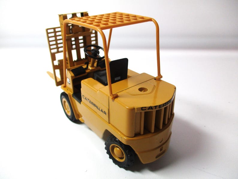 Może przedstawiać: Ż&oacute;łta zabawka w&oacute;zka widłowego Caterpillar z czarnymi oponami i czarnym siedzeniem. W&oacute;zek widłowy ma ochronną konstrukcję nad głową, a na boku widnieje napis "CATERPILLAR".