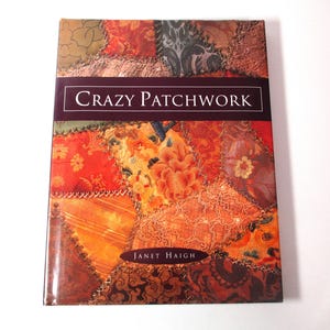 May include: A book titled "Crazy Patchwork" with a colorful patchwork design cover. The cover features a variety of fabric patterns in shades of orange, red, brown, and green. The author's name, Janet Haigh, is also visible.