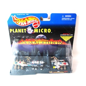 May include: A Hot Wheels Planet Micro Armageddon Mission 7 Asteroid Drill Site playset in original packaging. The set includes miniature space vehicles and rocky terrain pieces displayed behind a clear plastic blister on a blue and black card.