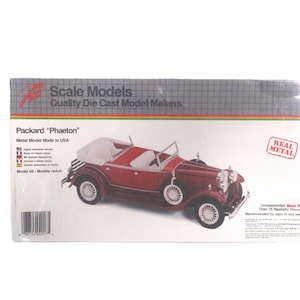 May include: A boxed scale model of a Packard "Phaeton" convertible car. The model is red with white accents and white tires. The box reads "Scale Models" and "Real Metal". The model kit is recommended for ages 10 and over.