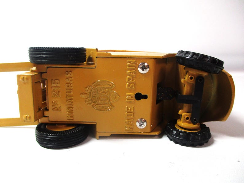 Może przedstawiać: Ż&oacute;łta zabawka, pojazd budowlany, do g&oacute;ry nogami, z czarnymi oponami. Sp&oacute;d zawiera napis "MADE IN SPAIN" i "N&ordm; 215 MINIATURAS". Zabawka ma szczeg&oacute;łowy design i jest wykonana z metalu.