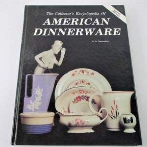 May include: The Collector's Encyclopedia of American Dinnerware book cover with a black background and a white title. The cover features a figurine of a man in a top hat, a pitcher, a bowl, a gravy boat, and a vase. The book is a guide to collecting American dinnerware.