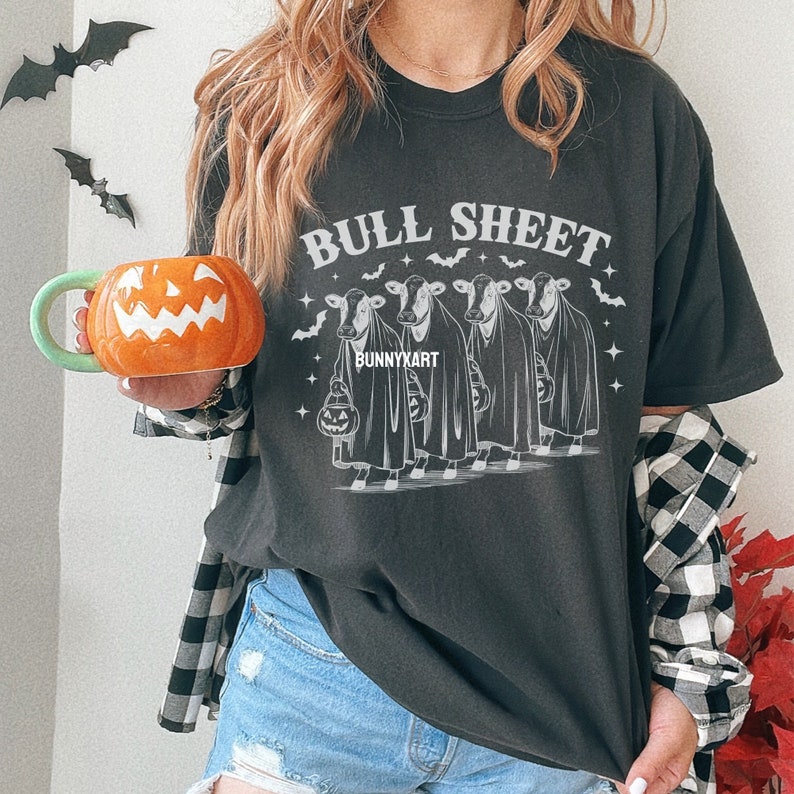 May include: Dark gray t-shirt with the text "BULL SHEET" above a graphic of four cows dressed as ghosts, holding jack-o'-lanterns. The shirt has a Halloween theme with bats and stars. The brand name "BUNNYKART" is also visible.