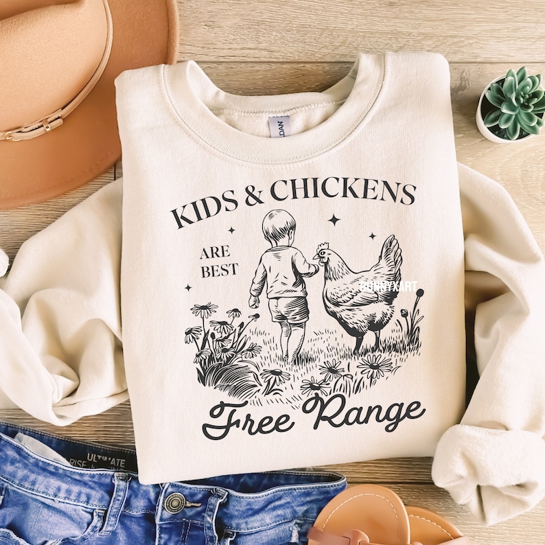 May include: A cream-colored sweatshirt with a black graphic design of a child and a chicken. The text reads "Kids & Chickens Are Best Free Range".