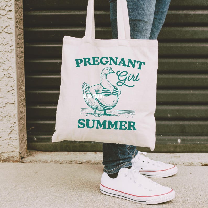 May include: A white tote bag with a green graphic of a pregnant duck wearing a bikini and the text "Pregnant Girl Summer".
