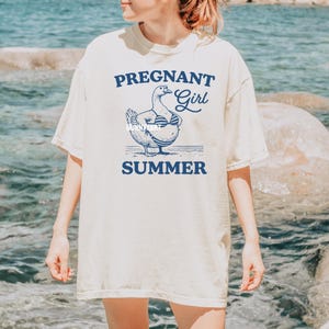 May include: A white t-shirt with a blue graphic of a pregnant duck wearing a bikini and the text "Pregnant Girl Summer".