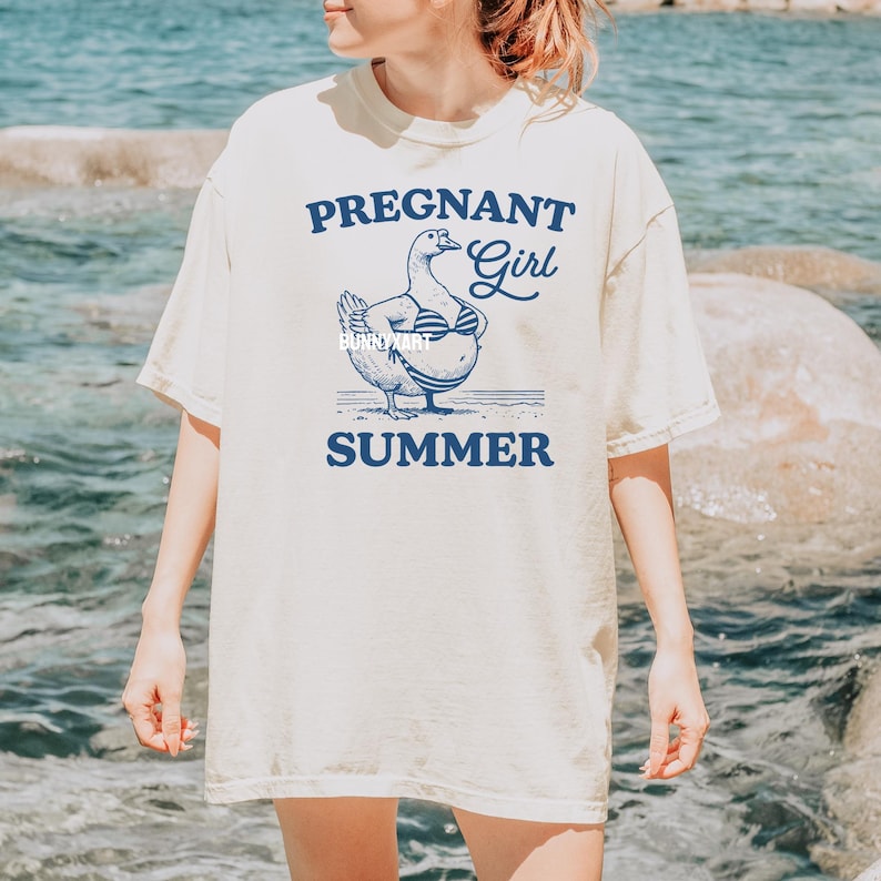 May include: A white t-shirt with a blue graphic of a pregnant duck wearing a bikini and the text "Pregnant Girl Summer".