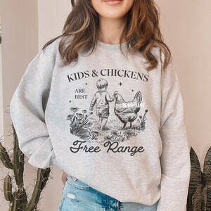 May include: Gray sweatshirt with a black graphic design of a child holding a chicken's wing. The text reads "Kids & Chickens Are Best Free Range".