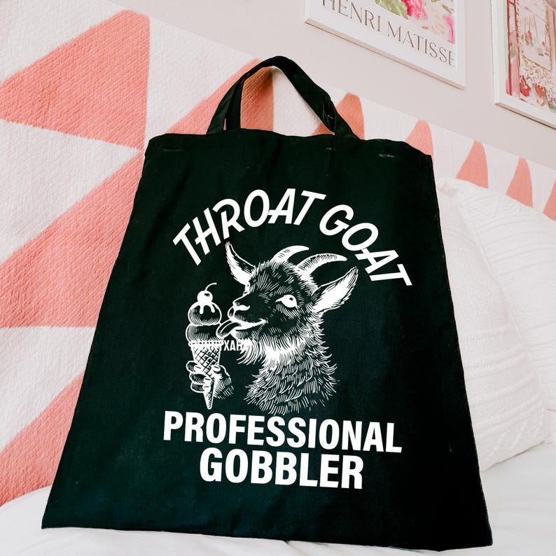 May include: Black tote bag with a white graphic of a goat eating ice cream. The text on the bag reads "Throat Goat Professional Gobbler".