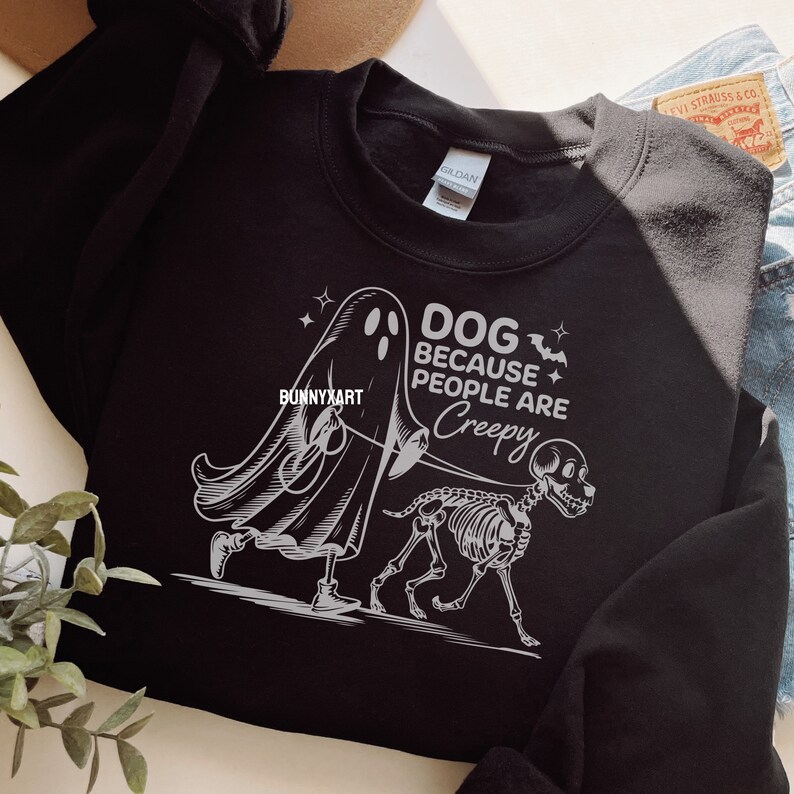 May include: Black sweatshirt featuring a white graphic of a ghost walking a skeleton dog on a leash. The text reads "DOG BECAUSE PEOPLE ARE CREEPY" with bat and star accents. A brand tag is visible.