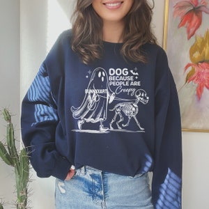 May include: Navy blue sweatshirt featuring a white graphic of a ghost and a skeleton dog. The text on the sweatshirt reads "DOG BECAUSE PEOPLE ARE CREEPY" and "BUNNYXXART". The sweatshirt is worn by a person.