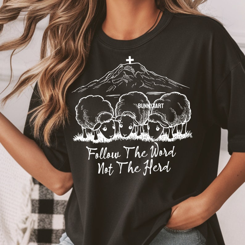 May include: Black t-shirt with a white graphic of a mountain with a cross on top and three sheep in front of it. The text "Follow The Word Not The Herd" is below the sheep.