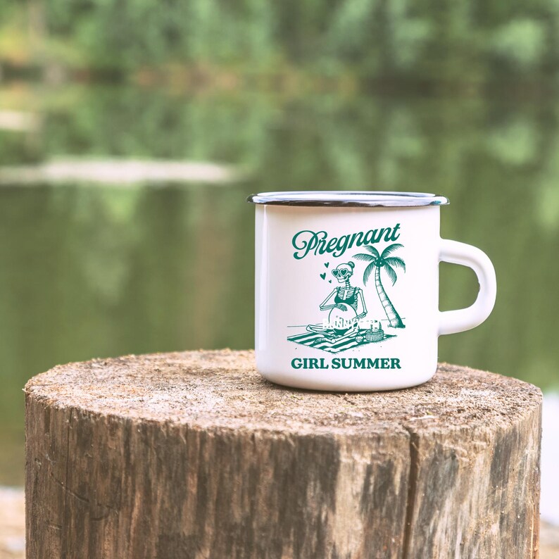 May include: White enamel camping mug with a black rim. The mug features a green graphic of a skeleton wearing a bikini and sunglasses, holding a beach ball. The text "Pregnant Girl Summer" is printed on the mug.